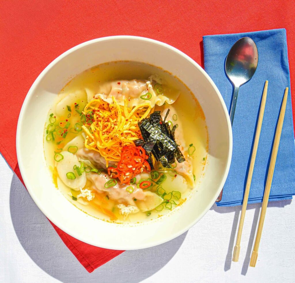A comforting soup of rice cakes, dumplings, and fresh vegetables, topped with egg yolk ribbons and nori