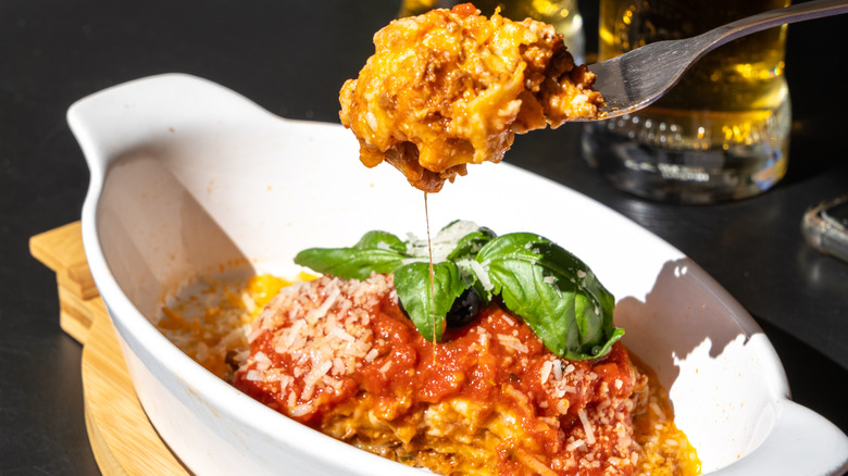 Lasagna in a baking dish, with a fork pulling out a gooey slice