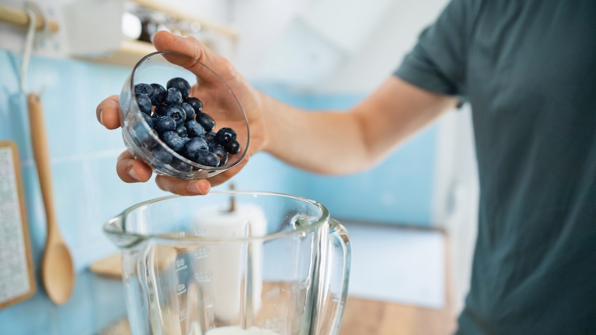 Man putting blueberries in smoothie - healthy eating