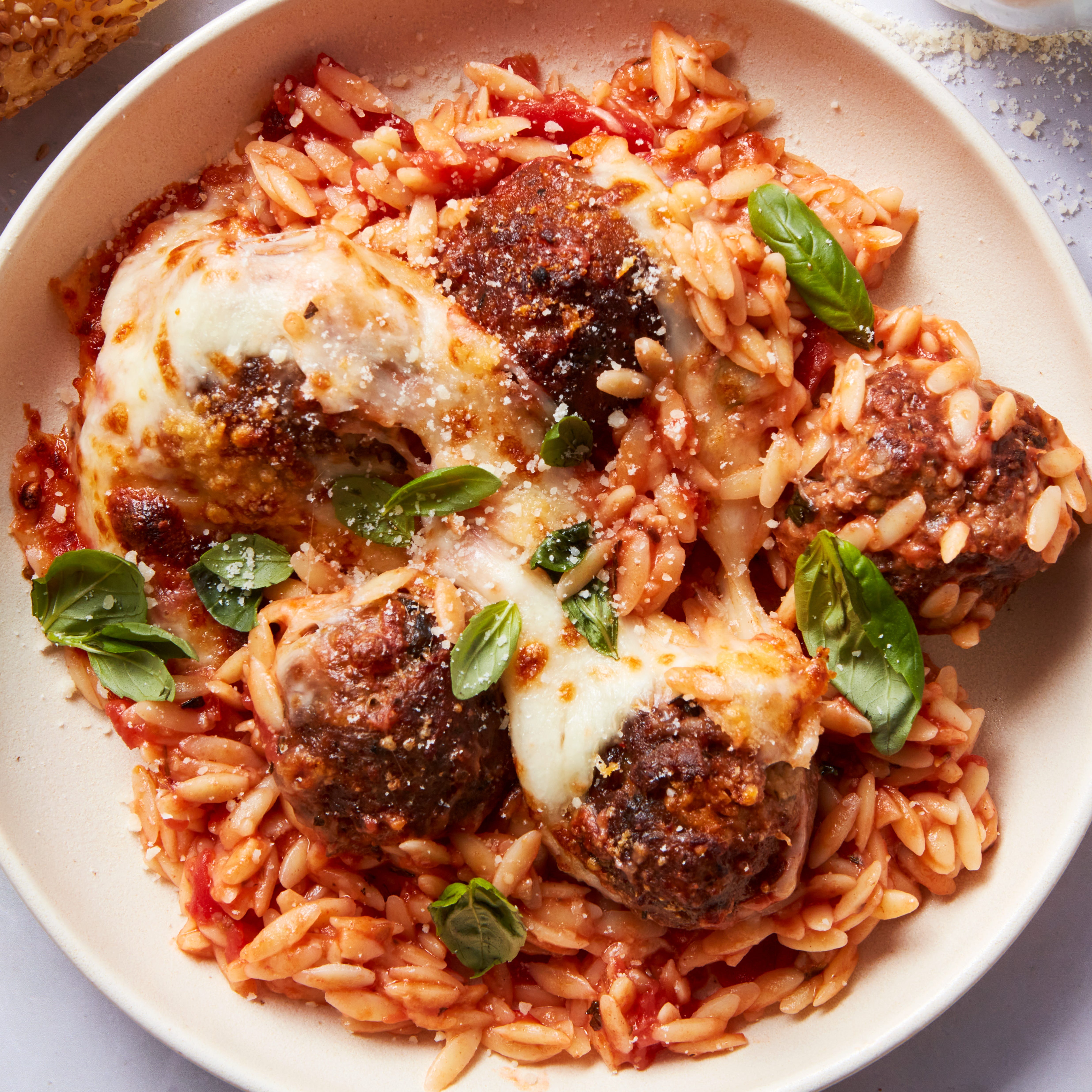 tomato based orzo in a skillet topped with meatballs and cheese