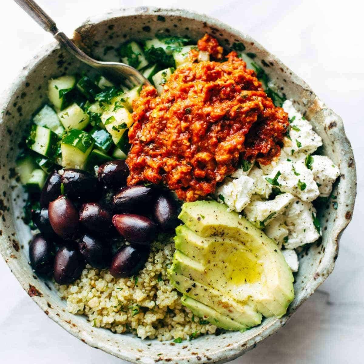 a bowl with quinoa, avocado, olives, feta cheese, and cucumbers