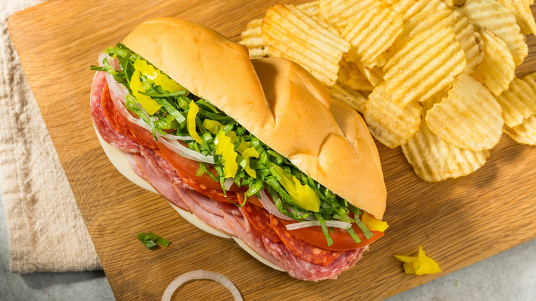 An Italian sub with chips on a cutting board.