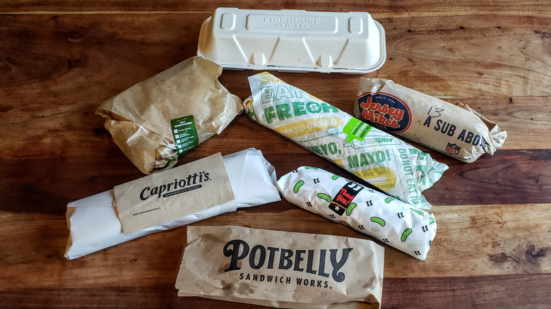 Seven different Italian sub sandwiches on a wooden table.