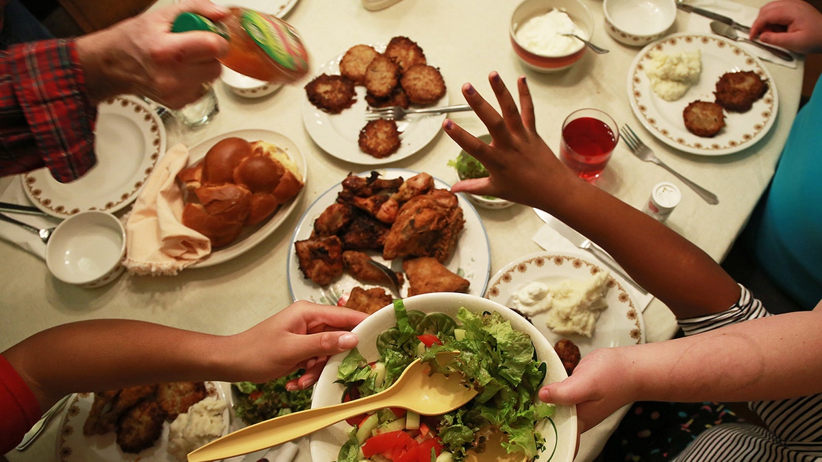 Family passes salad and dressing around dinner table, hands seen reaching and grabbing over food.
