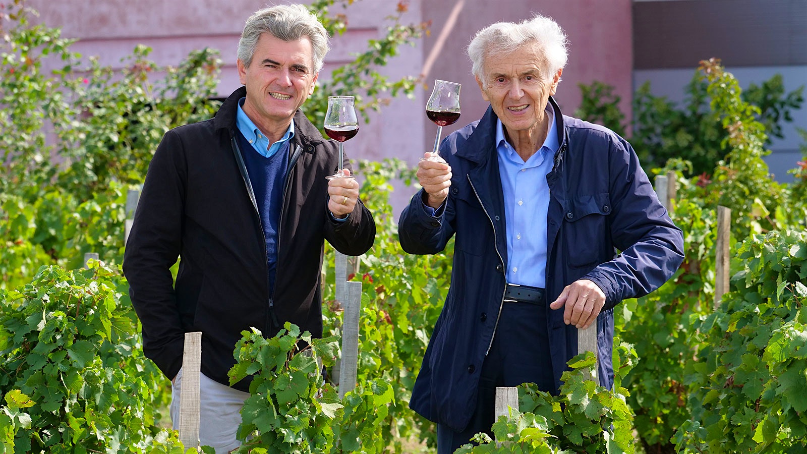 Franck and Georges Duboeuf with glasses of red wine in a vineyard