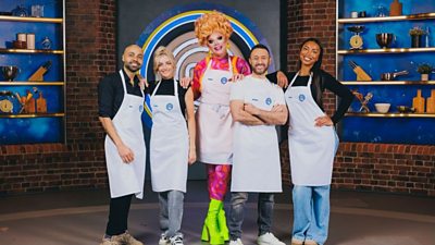 A group image of five Celebrity MasterChef contestants wearing white aprons in the exposed brick MasterChef kitchen. Cooking equipment lines the shelves behind them.