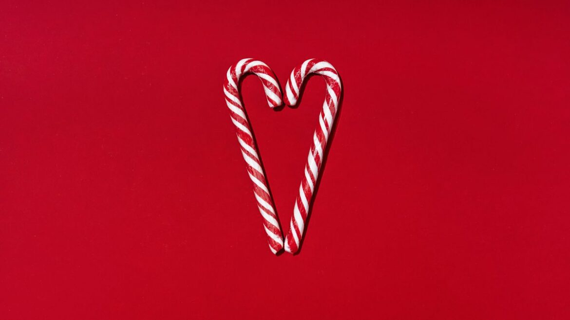 Two candy canes facing each other to form a heart shape. On a deep red background