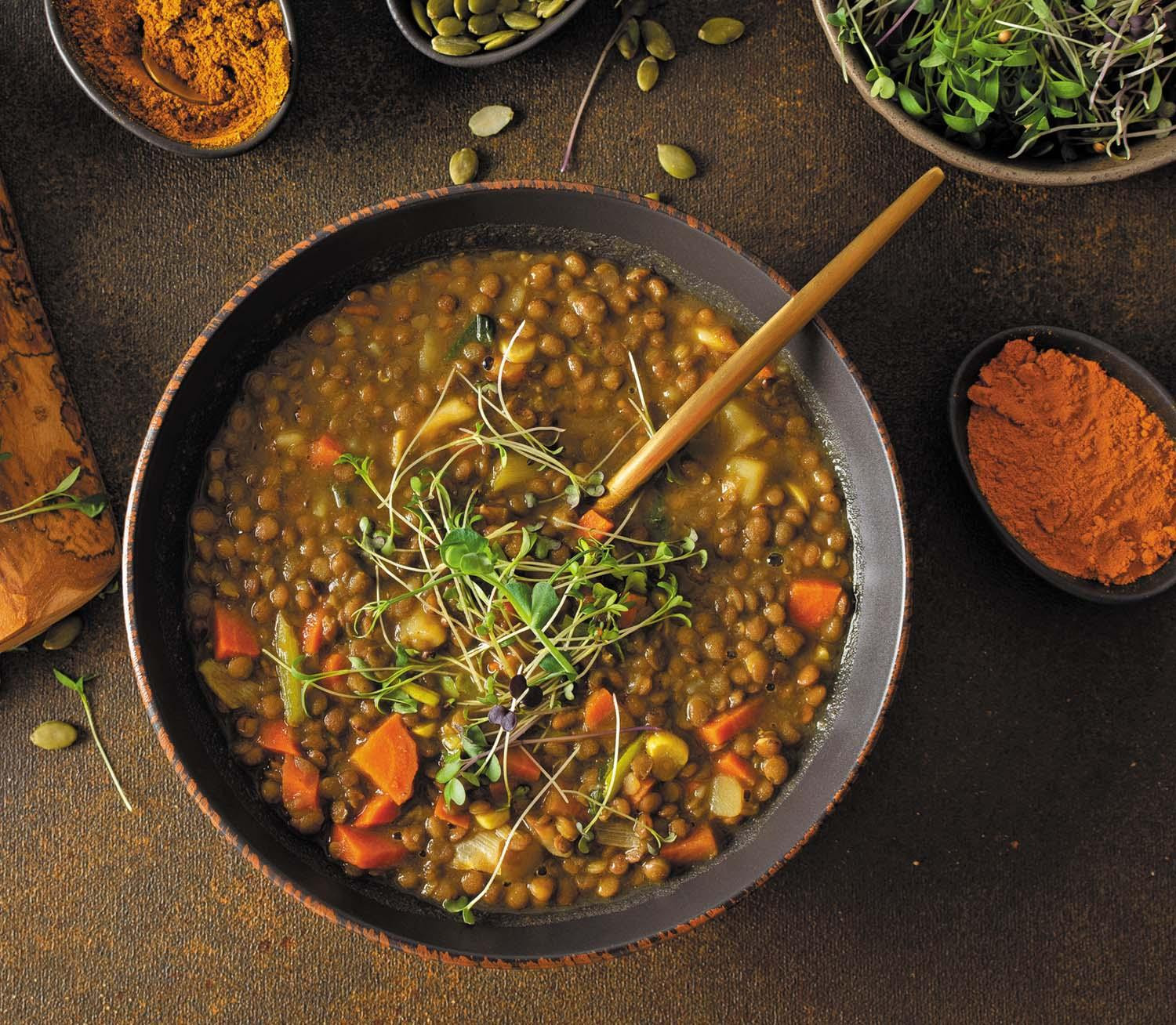 Overhead view of a bowl containing red lentil dal, an Indian stew rich in fiber, with a wood serving spoon in the dish.