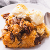 a close up of one serving of pecan pie cobbler topped with ice cream on a white plate