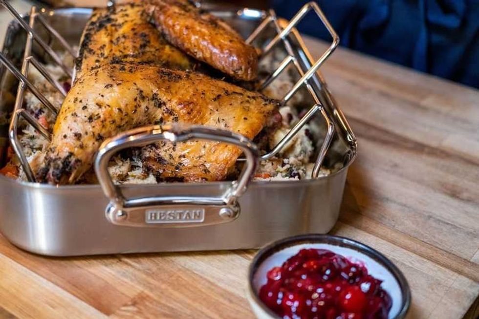 Roasted chicken on a rack in a pan, with stuffing and cranberry sauce on a wooden table.