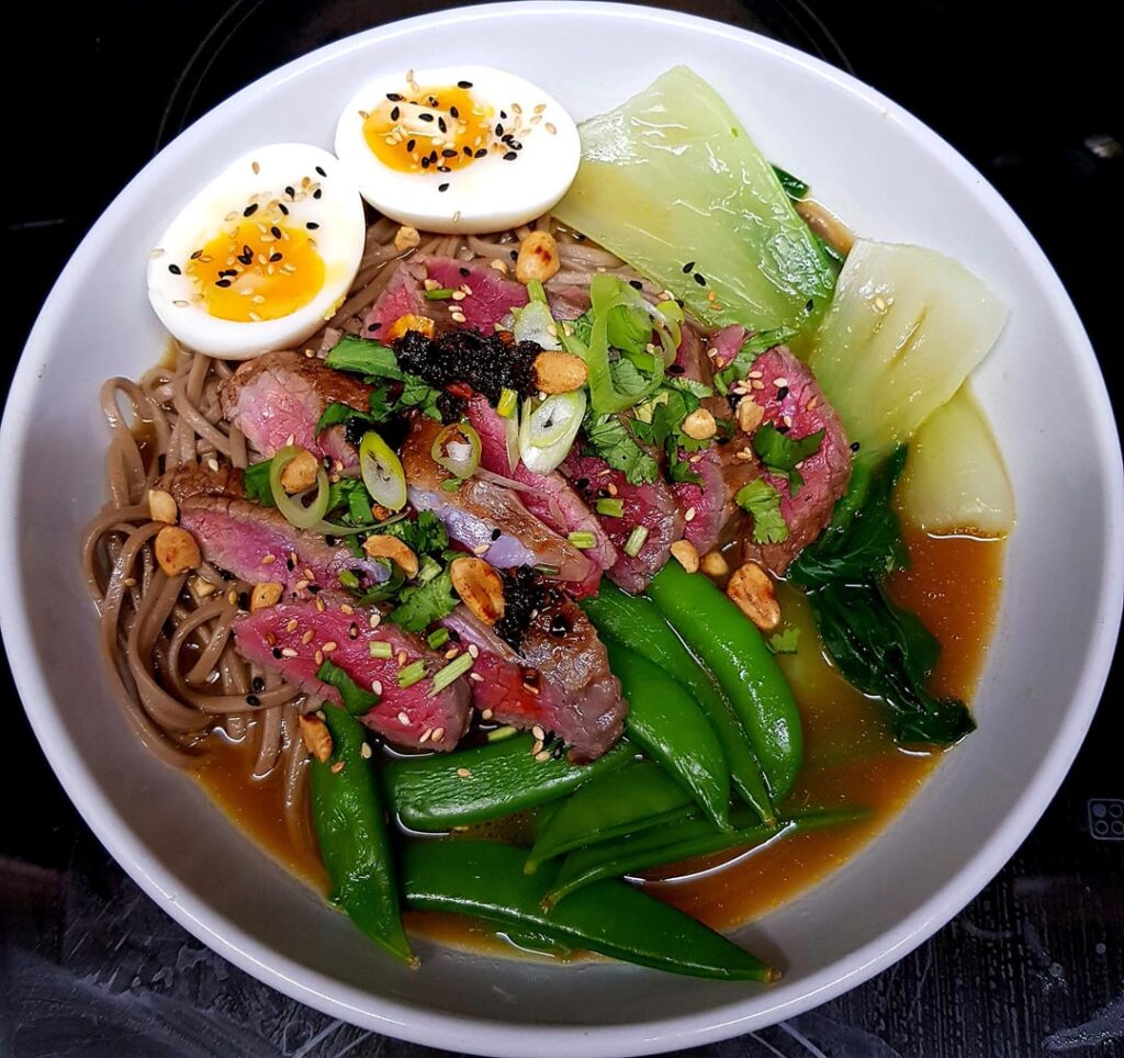 Asian Ginger, Chilli and Orange Broth with Soba Noodles and Greens. Rare Steak, Soft Boiled Egg, Herbs, Nuts and Seeds.