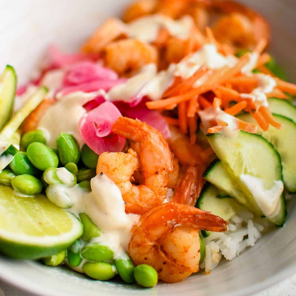 a bowl with rice, edamame, lime, carrots, and seared shrimp