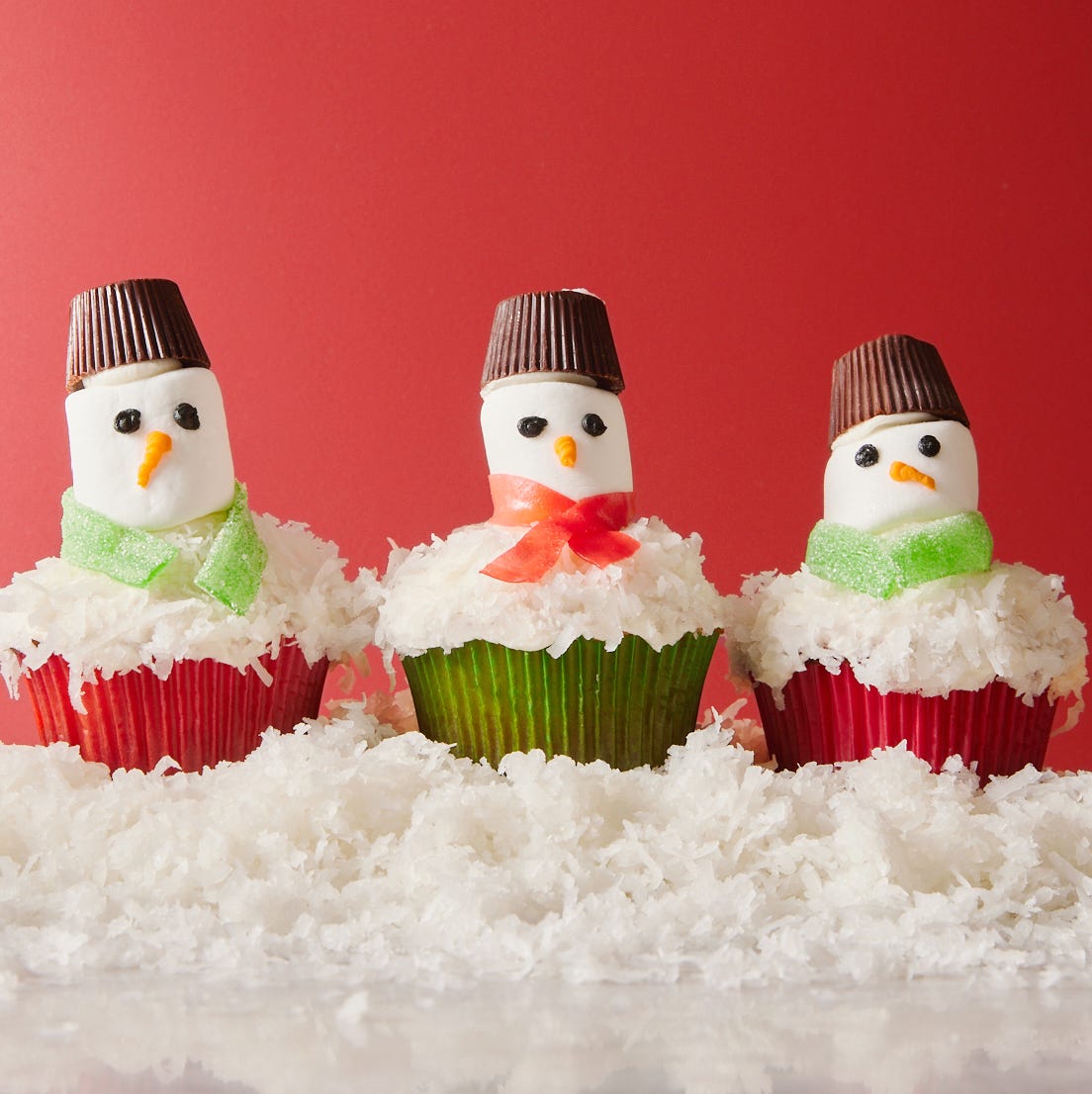 snowman cupcakes topped with shredded coconut snow, marshmallow faces, candy scarves, and peanut butter cup hats
