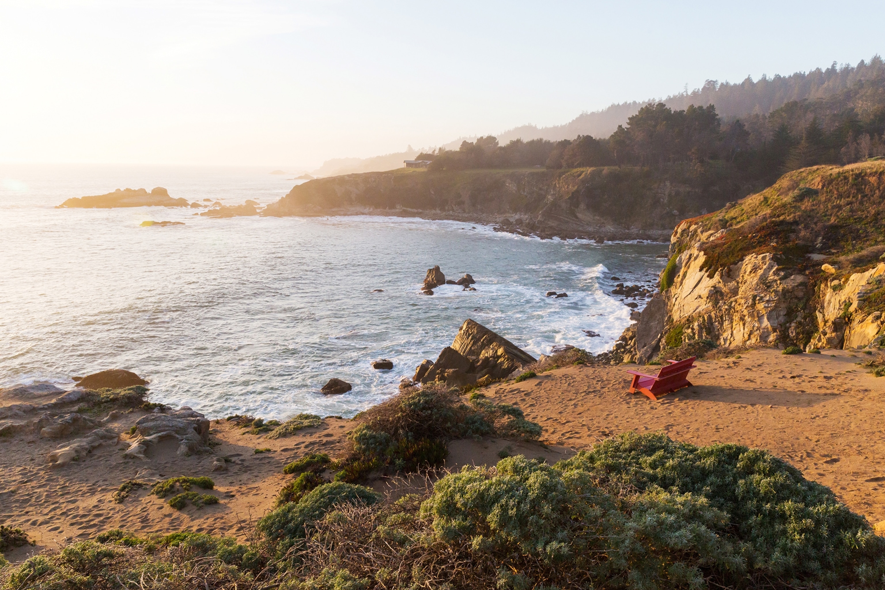 An epic landscape shot of a rock-lined coastline and a beach surrounded by low greenery.