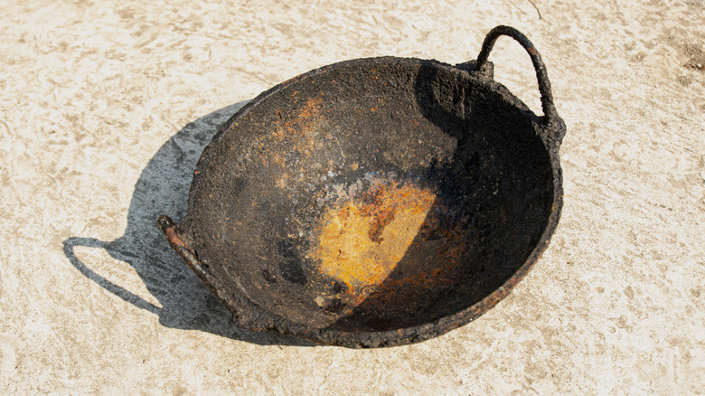 A rusted and corroded cast iron wok in the outdoors.