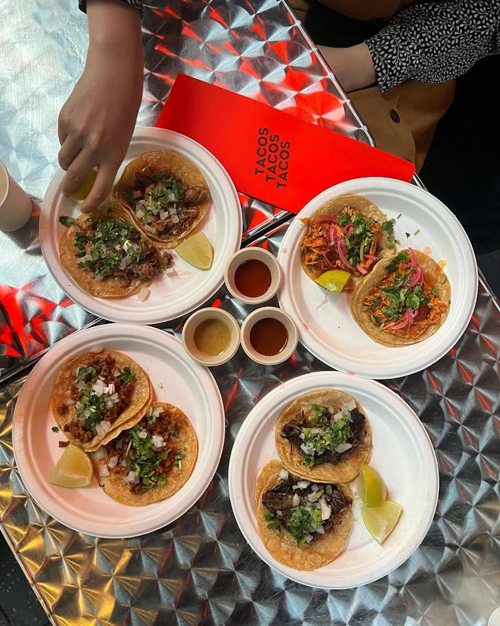 tacos tacos tacos potts point four plates of tacos and seasonings on a table, hands reach in to grab them