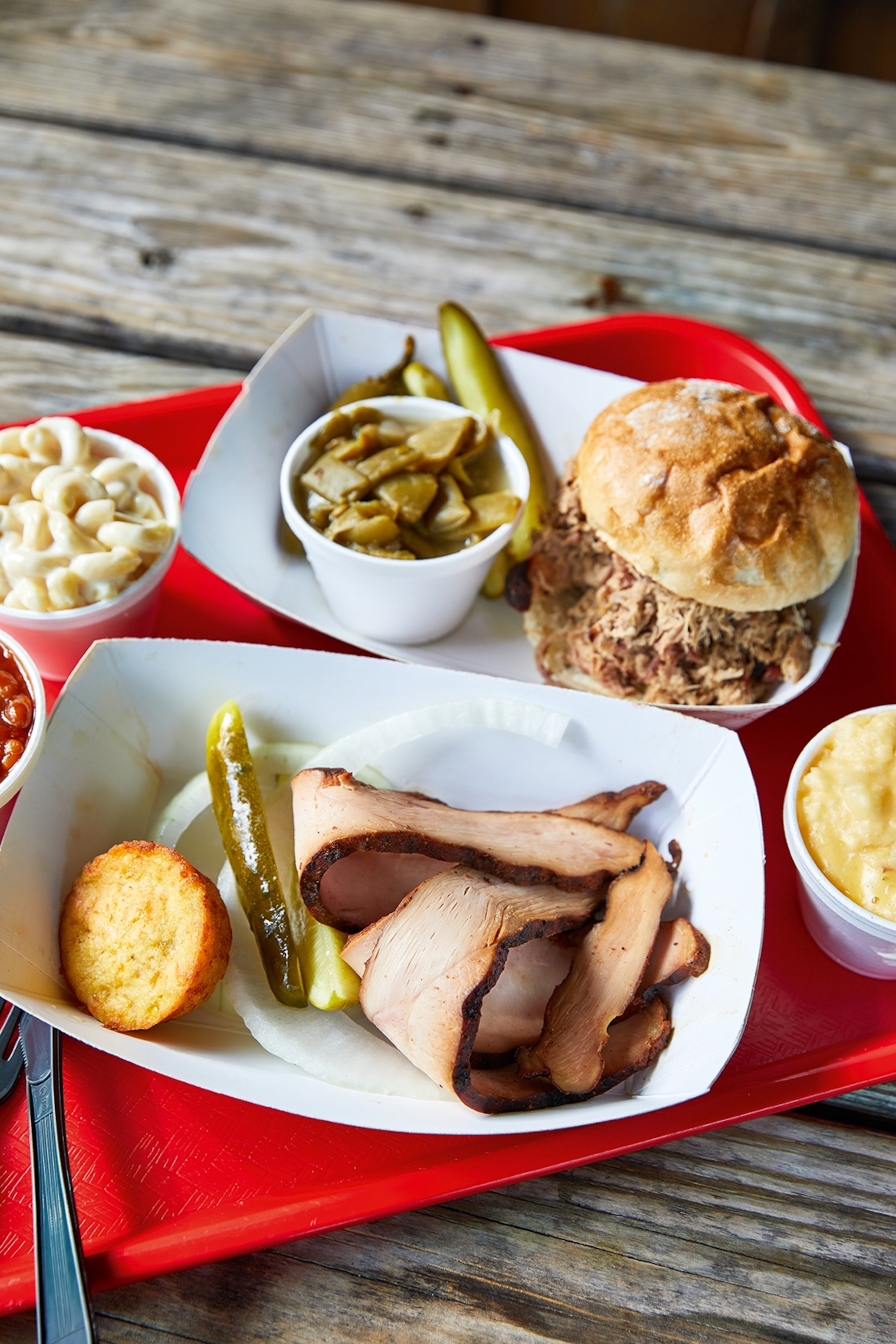 A close-up of street food on a tray, including pulled pork burgers and turkey strips with pickles.