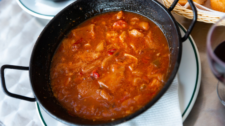 thin tomato broth with chunks of meat and vegetables cooked in cast iron wok