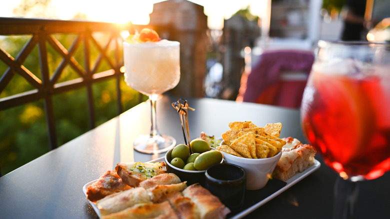 Delicious aperitivo with cocktails, nachos, olives, and focaccia, enjoyed on a terrace at sunset