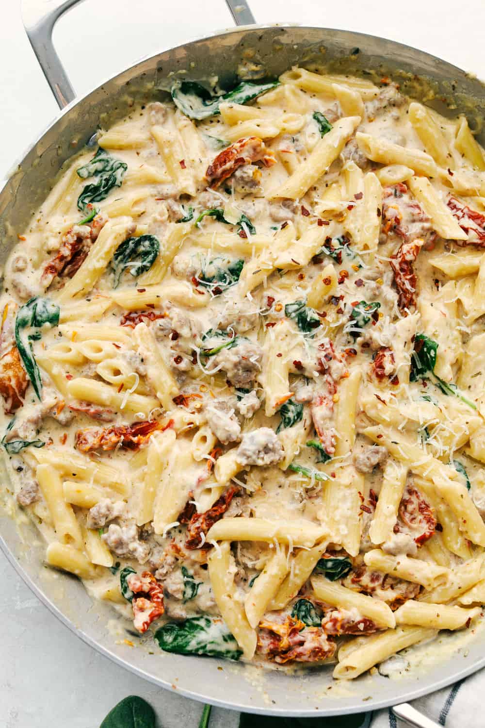 Creamy Tuscan sausage pasta is pretty much a one pan wonder you will want to cook over and over again! Perfect for a busy night, this is a hearty comforting dish that will truly satisfy. Creamy Tuscan Sausage Pasta in a pan garnished with parmesan cheese.
