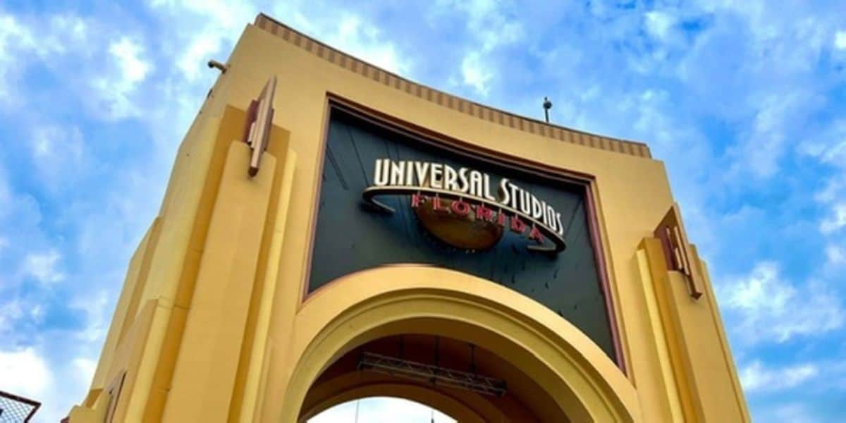 The photo shows the iconic yellow archway entrance of Universal Studios Florida, featuring the park's globe logo, where fans disappointed by a hyped attraction still gather under a partly cloudy blue sky.