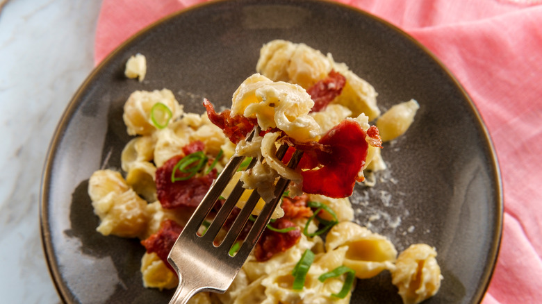 A fork holds a forkful of mac and cheese with cured ham
