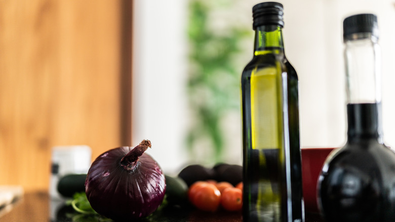 olive oil bottle on kitchen counter with onion and other veggies in the background