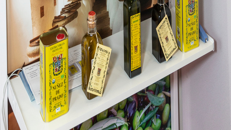 fancy extra virgin olive oil bottles lined on a shelf with an image of olive grove in the back