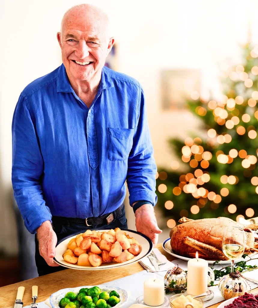 A man with food on a table in front of him and a Christmas tree behind.