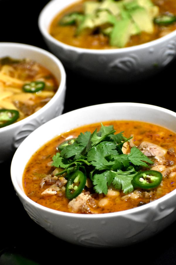 white bean turkey chili in three different bowls with different garnishings
