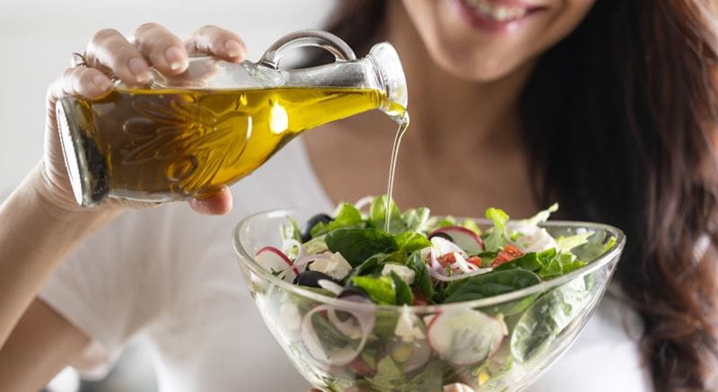 Woman smiling as she pours a bottle of olive oil on a leafy salad