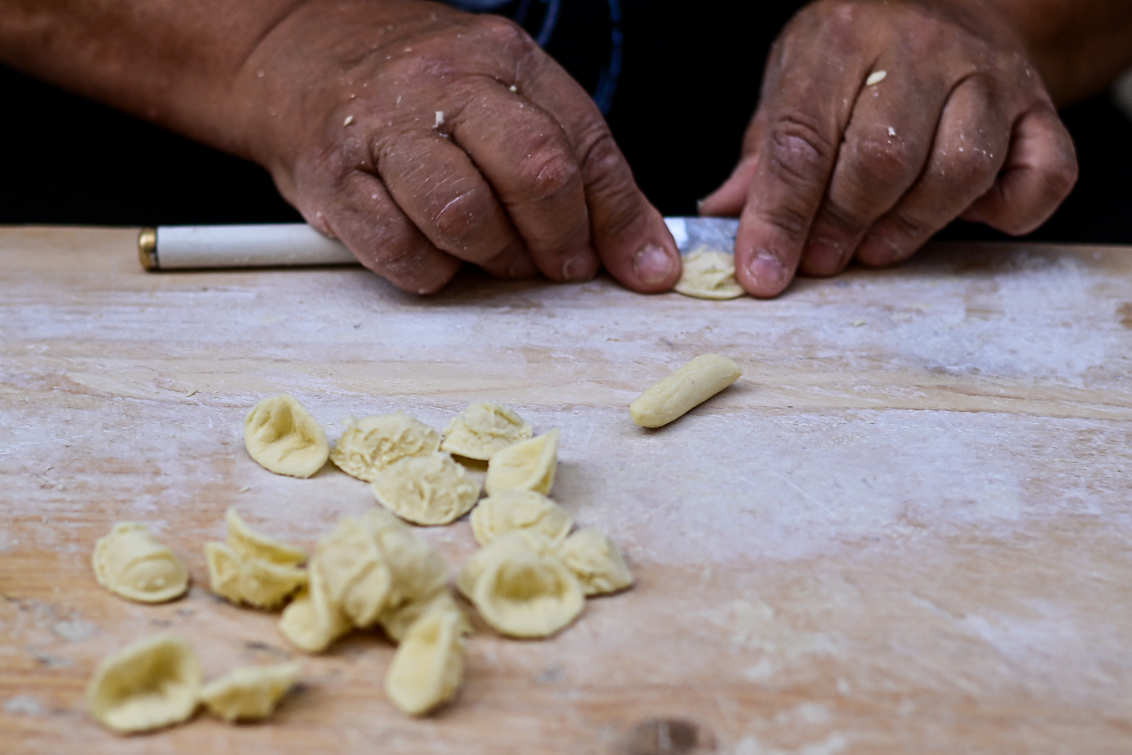 Hands preparing traditional orecchiette pasta on a wooden surface.