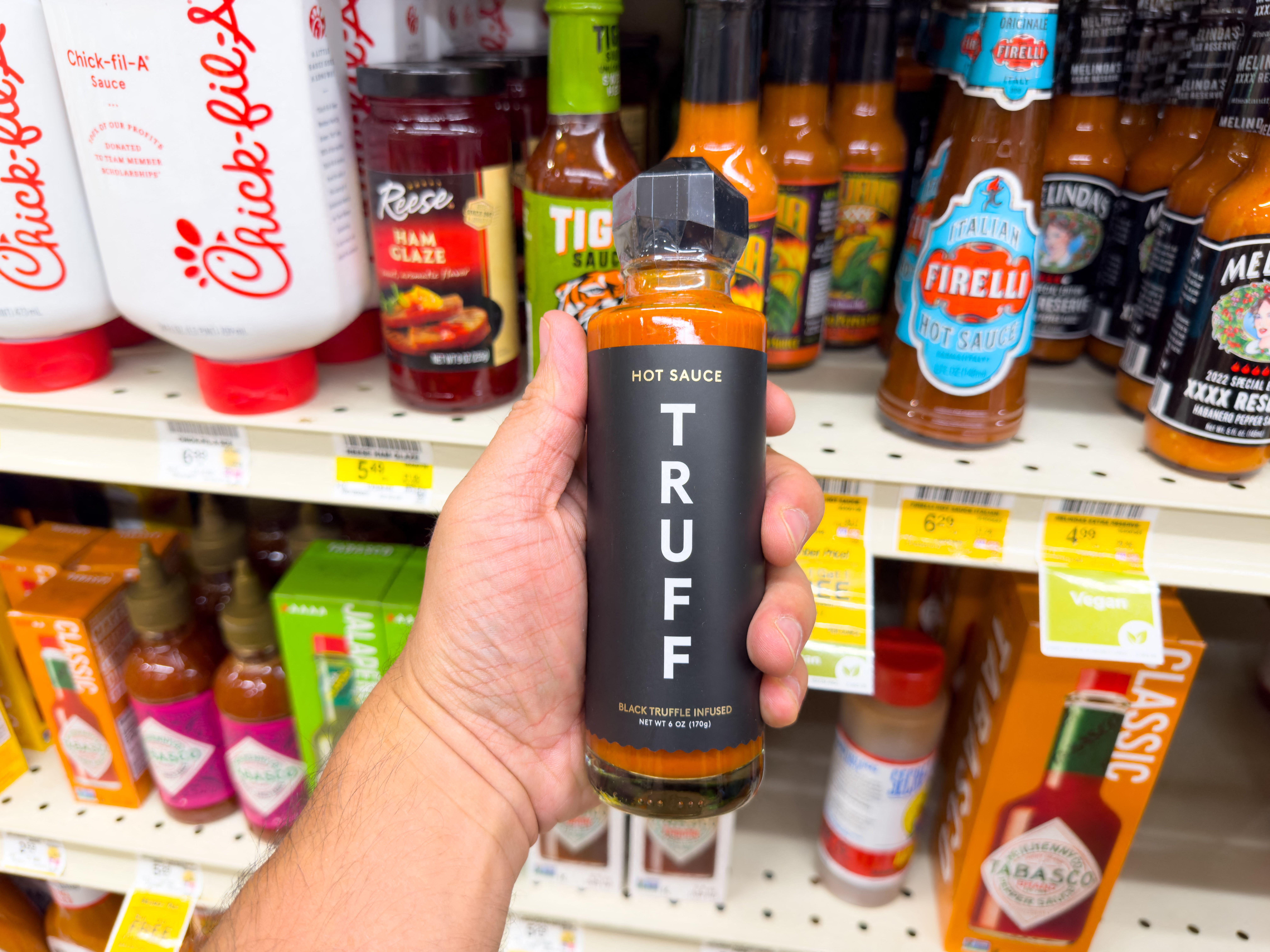A hand holding a bottle of Truff hot sauce in a store aisle.