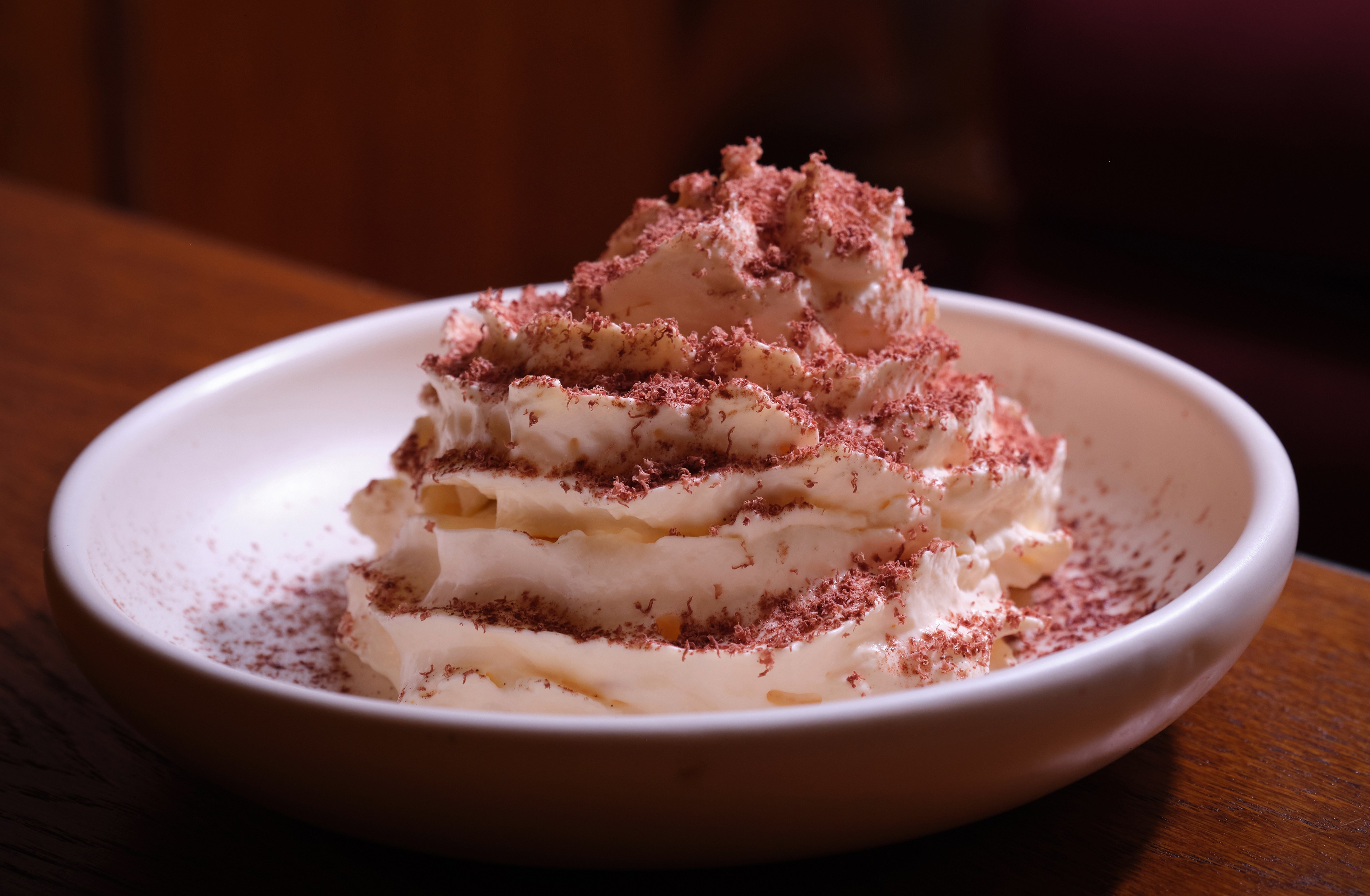 Tiramisu with whipped cream and chocolate shavings on a white plate.