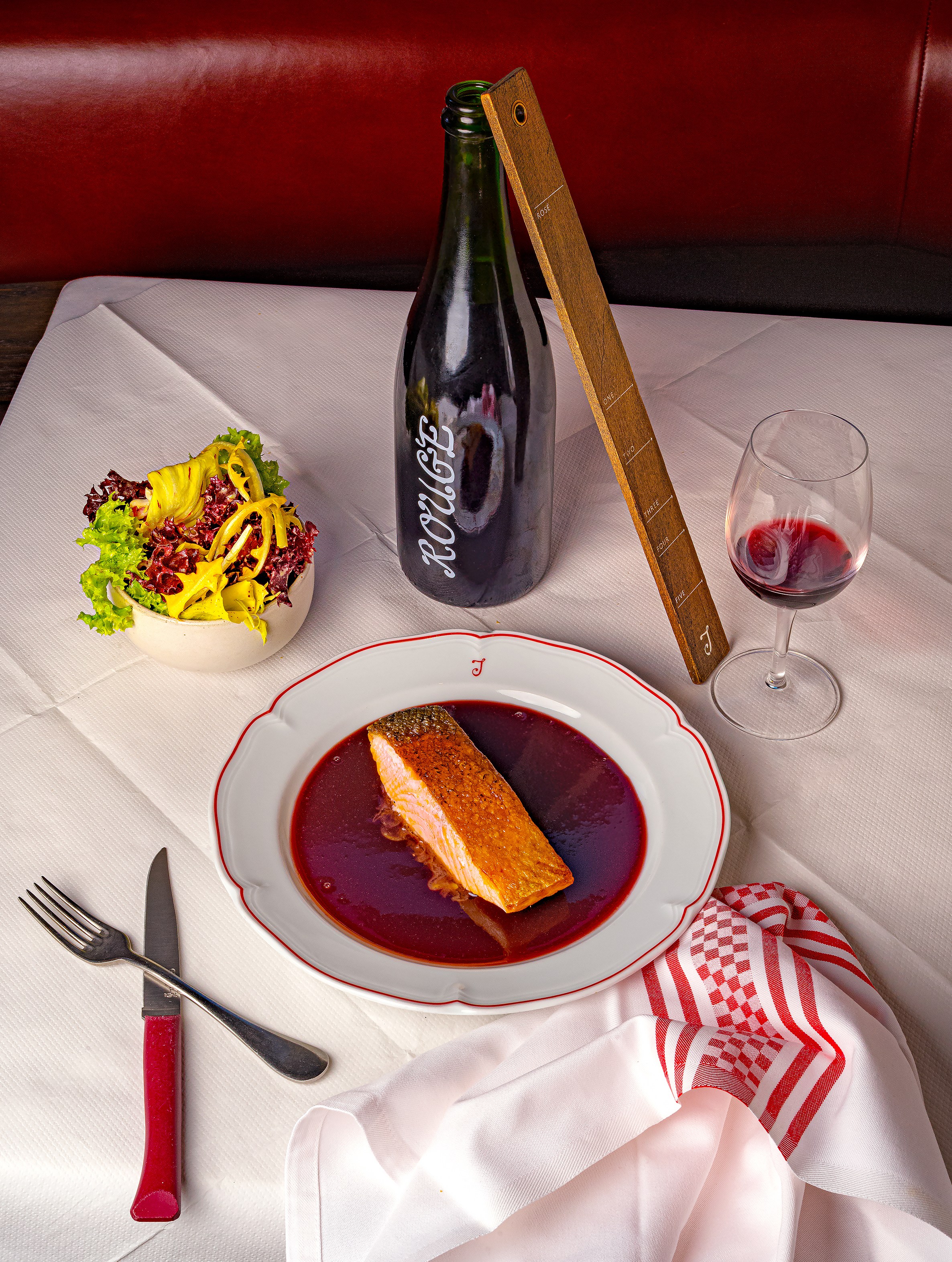 Salmon dish from Josephine bistro, with a salad, a bottle of wine, and a glass of red wine.