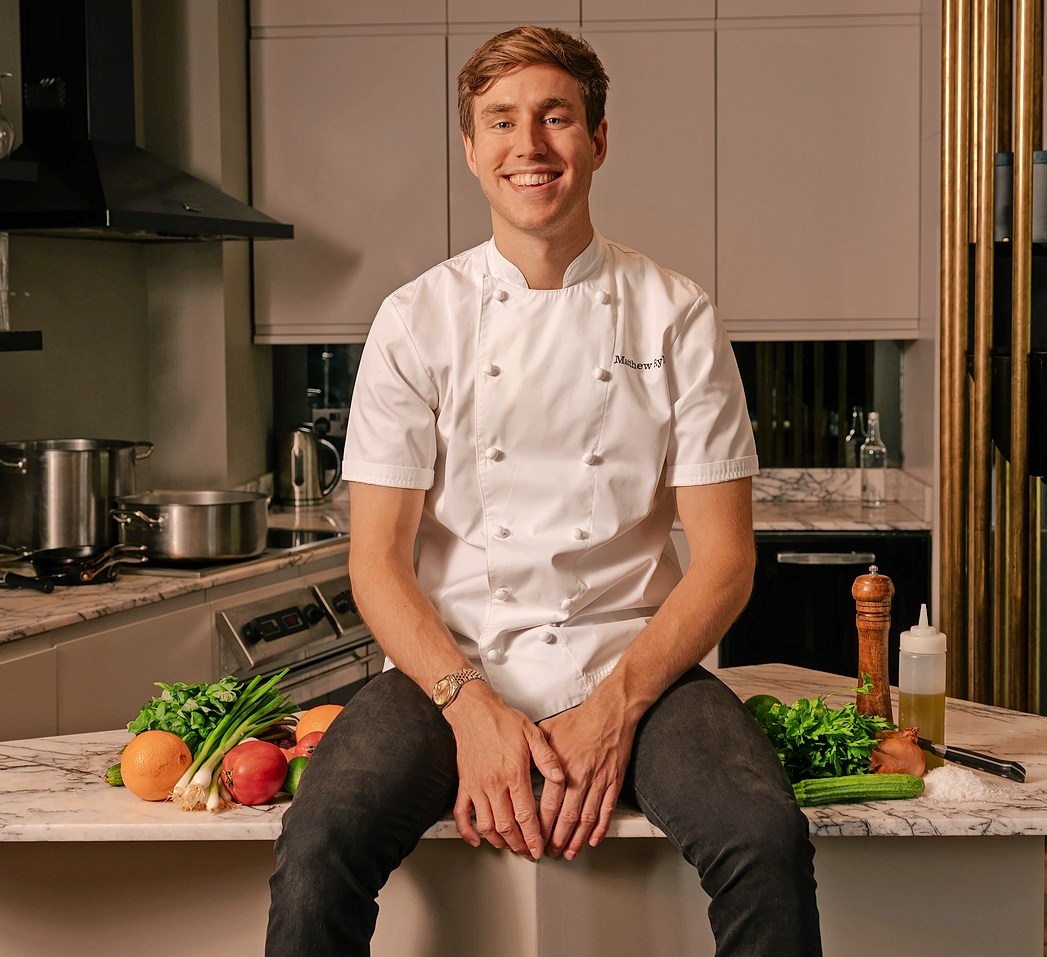 Matthew Ryle sitting on a kitchen counter with fresh produce.
