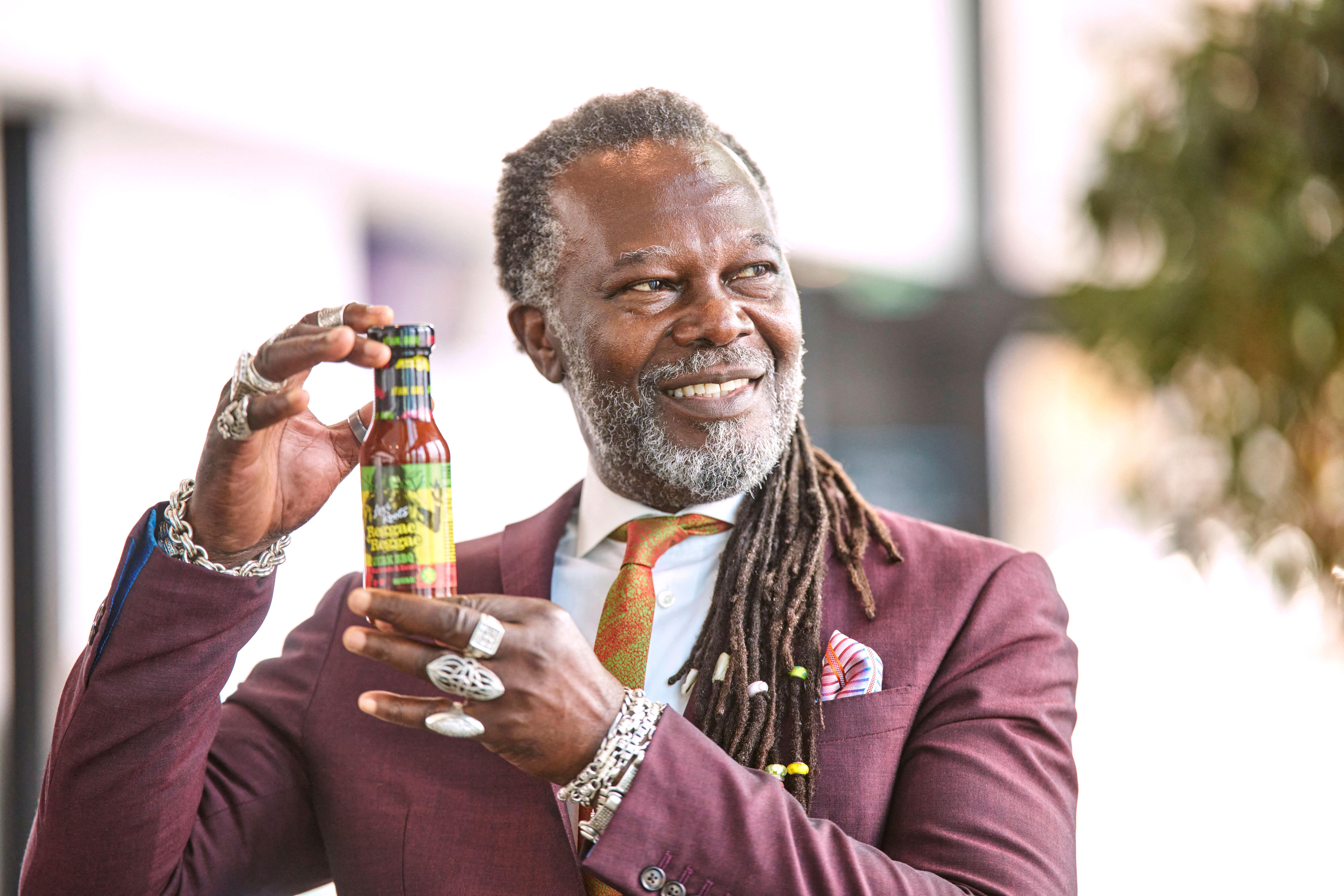 Levi Roots smiling and holding a bottle of Reggae Reggae sauce.