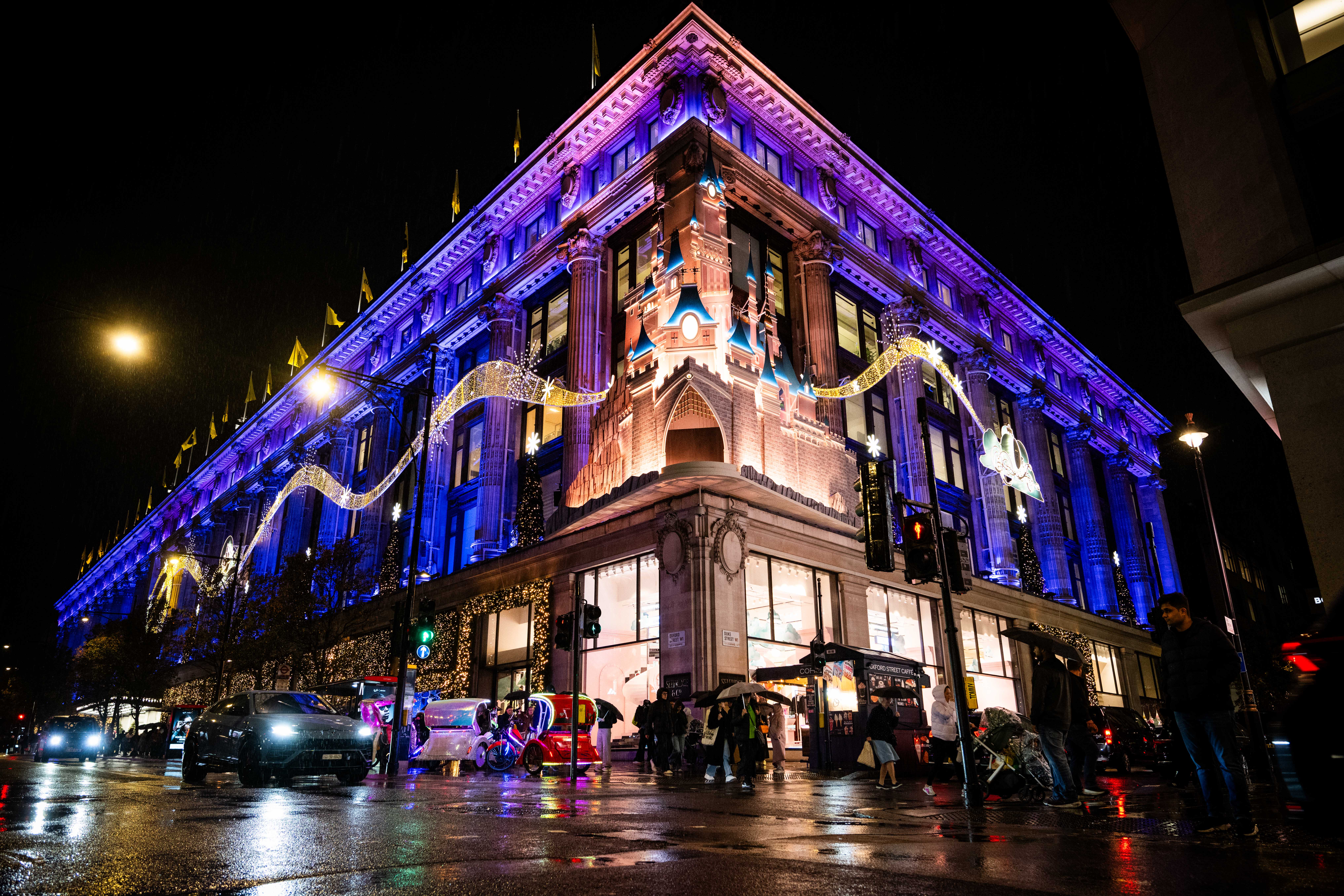 Selfridges department store in London illuminated with blue and purple lights and festive decorations at night.
