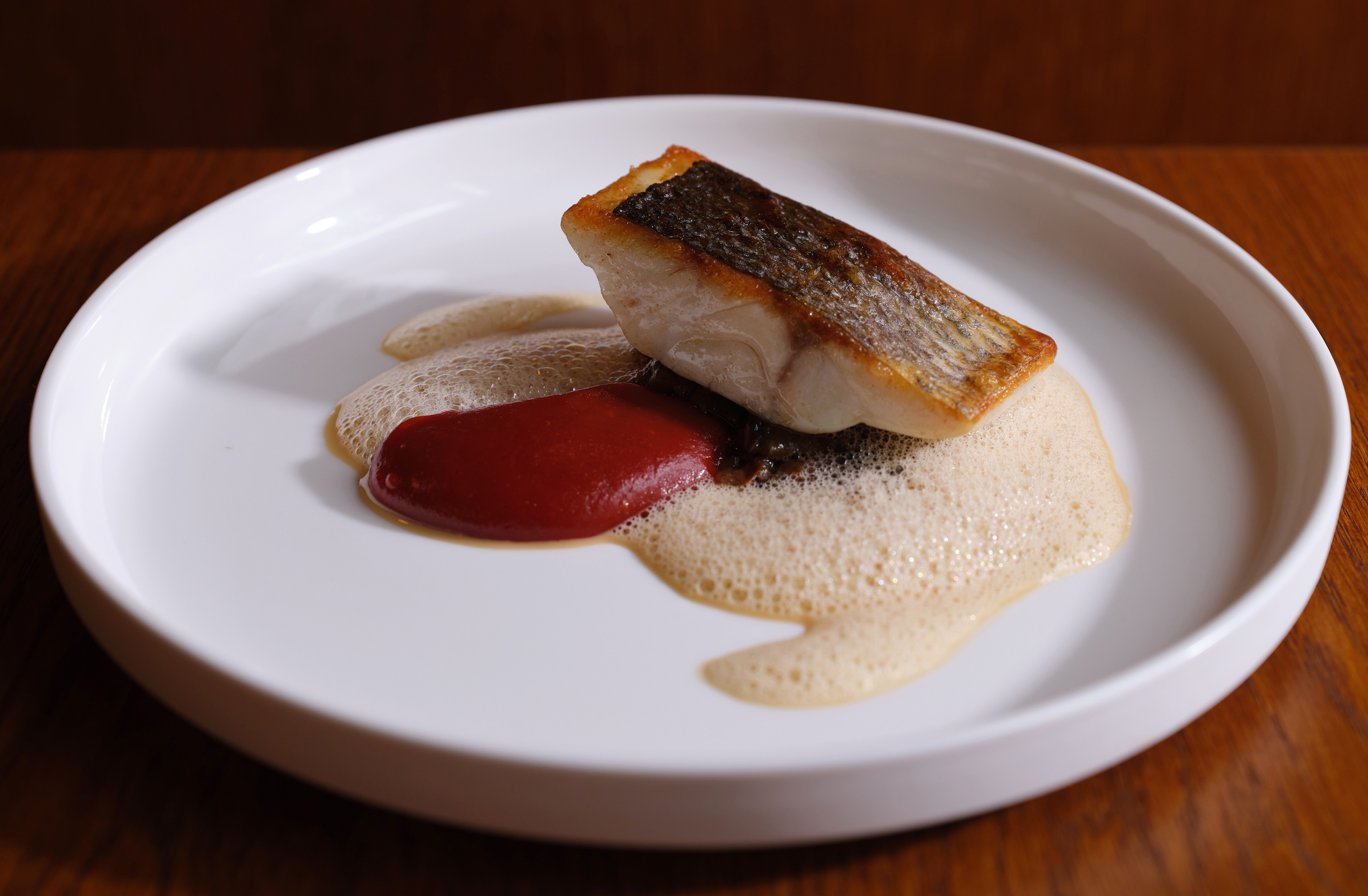 Seabass dish with a red sauce and foam on a white plate.