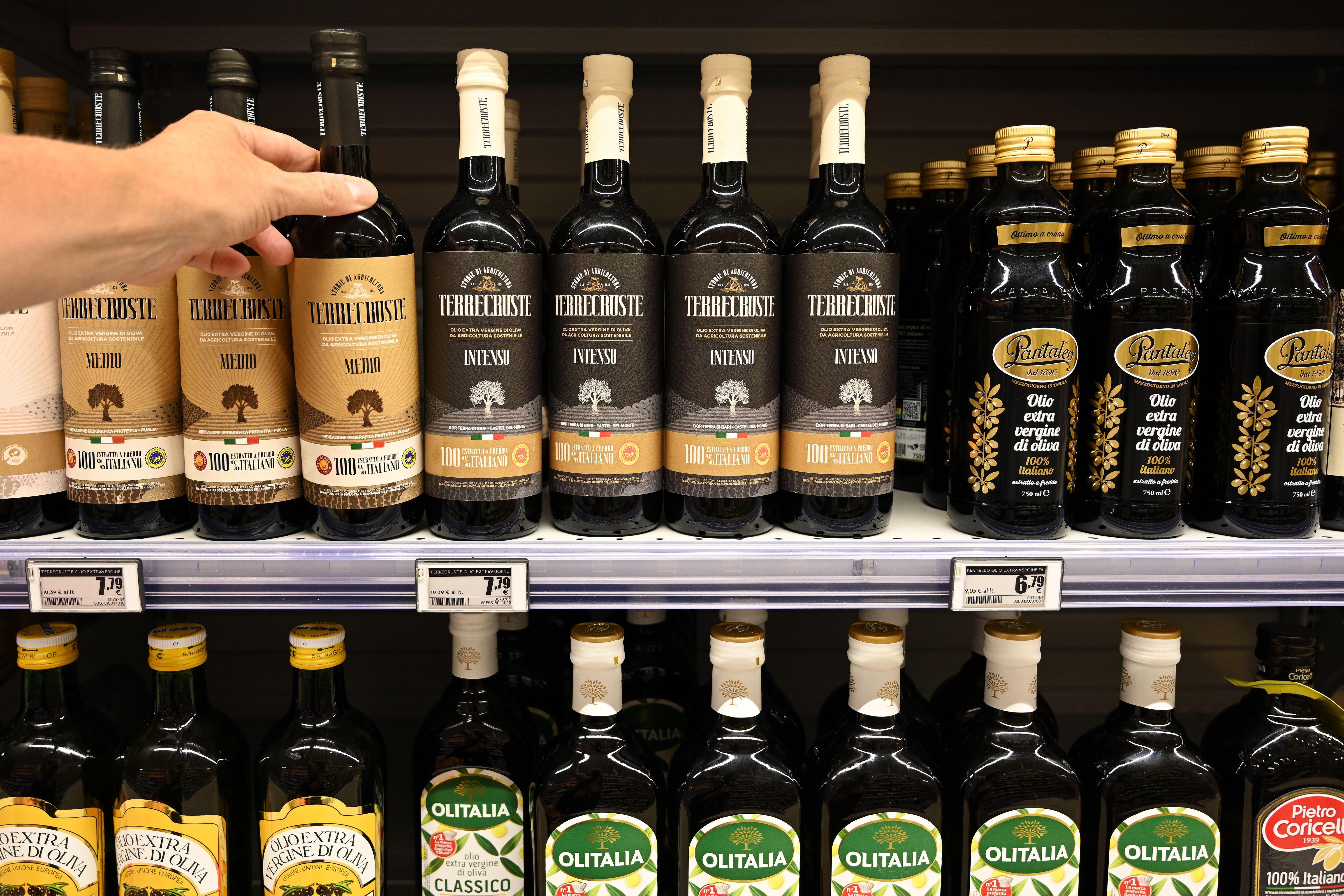 A hand reaching for a bottle of Italian olive oil on a store shelf.