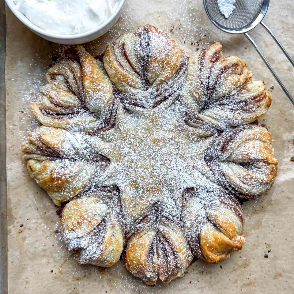 cinnamon roll snowflake puff pastry topped with powder sugar.