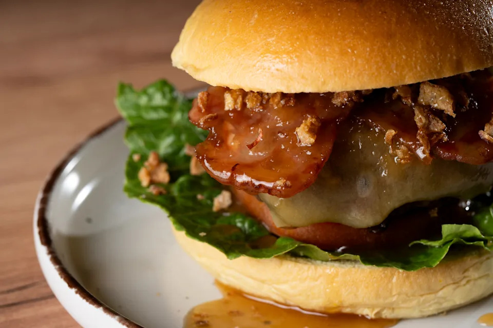 Close-up of a gourmet burger with crispy bacon, melted cheese, lettuce, and fried onion bits on a plate