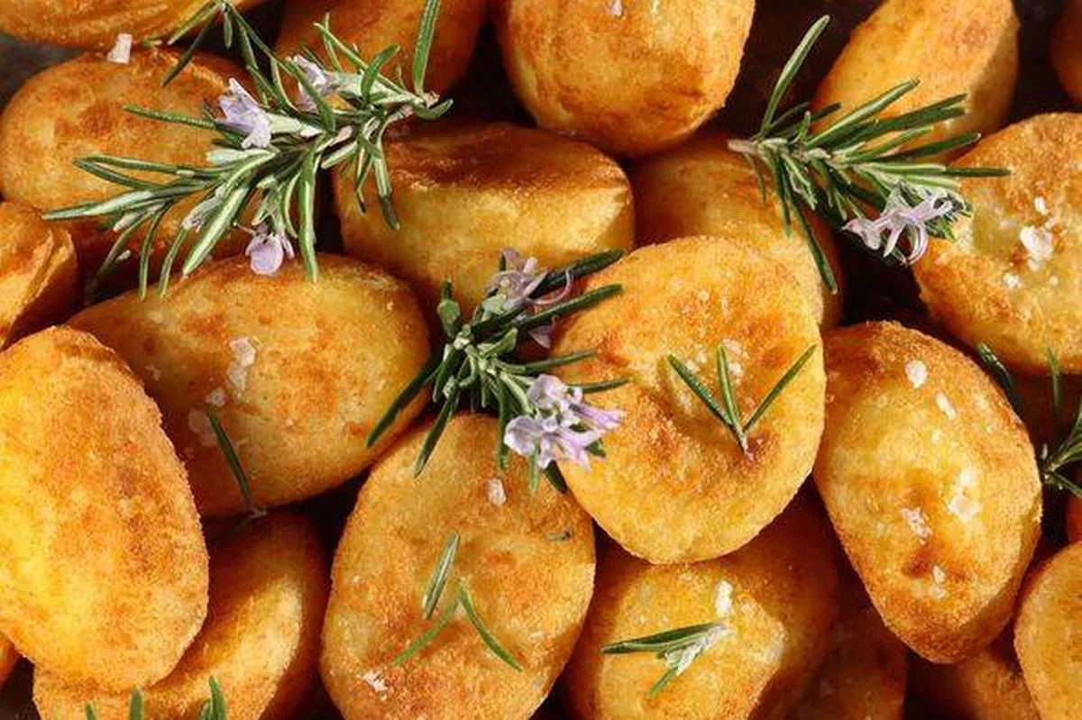 Full frame image of Christmas dinner or roast meal side dish, pile of crispy, golden roast potatoes, chunky salt flake seasoning, herb garnish of flow
