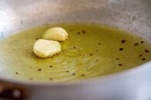 Garlic cloves sizzling in olive oil with chili flakes in a pan