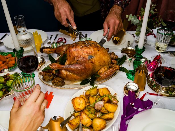 Man Carving Roasted Christmas Turkey At Dinner Table With Potatoes, Red Wine, And Candles