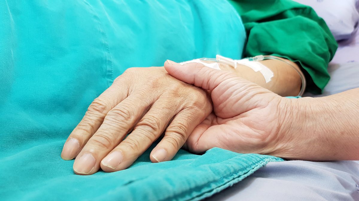 Woman holding a man's hand while laying in a hospital bed