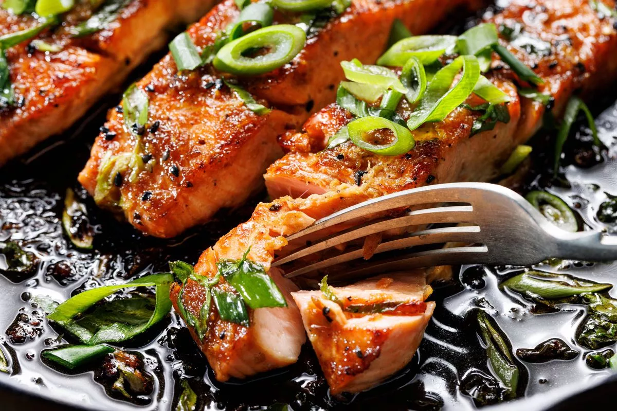 Close-up view of teriyaki salmon sprinkled with chopped scallion on a black background