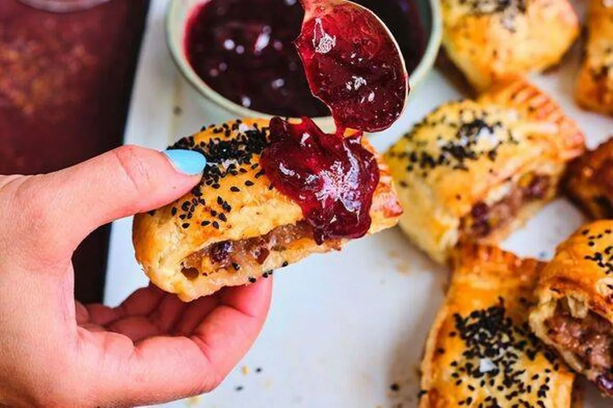 sausage roll covered in cranberry sauce being held by woman with blue nail polish