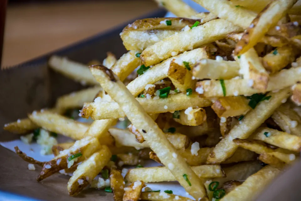 A close-up of crispy French fries topped with minced chives and grated cheese on a plate