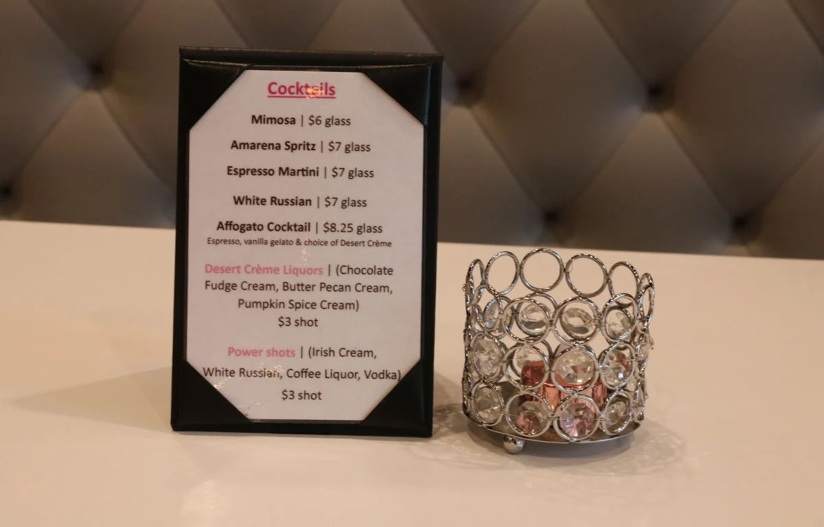 Countertop sign showing Le Macaron’s alcoholic beverage options and special offerings beside a decorative holder.